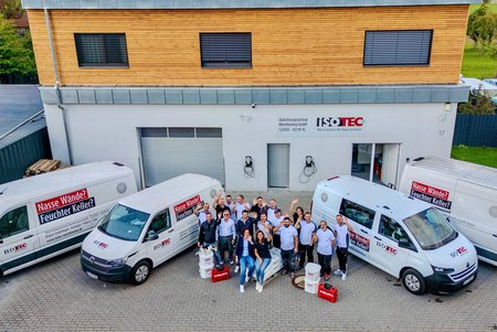 ISOTEC Team steht vor Firmengebäude mit Servicefahrzeugen
